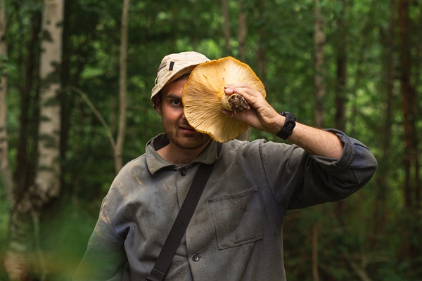 man holding giant milk agaric in front of his face after picking them in forest on a autumn day - Сбор, заготовка и переработка дикорастущих плодов, ягод и грибов