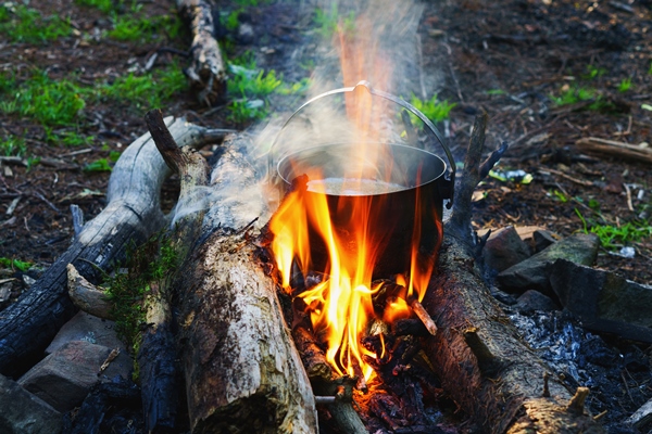 tourist bowler with food on bonfire cooking in the hike outdoor camping activities preparation of pilaf or soup on fire authentic adventures and survival concept - Пшеничная каша в котелке на костре