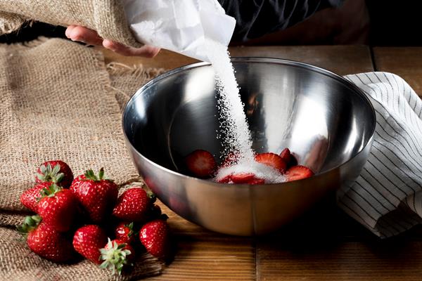 high angle of chef adding sugar to bowl of strawberries - Клубника, протёртая с сахаром