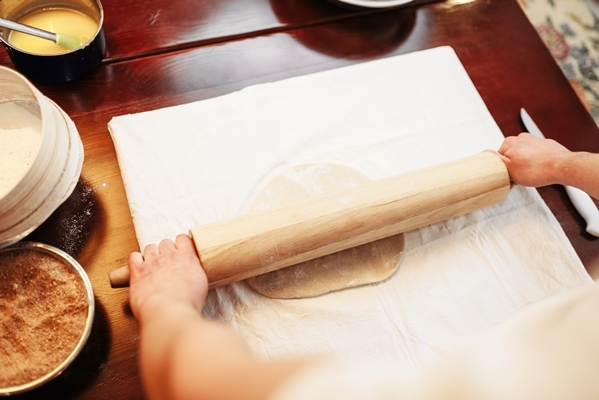 male chef roll out the dough with a rolling pin top view wooden kitchen table - Постный штрудель с яблоками, орехами, изюмом и корицей