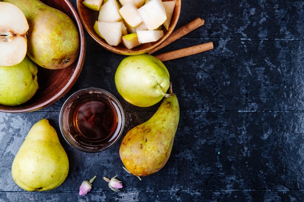 top view of fresh ripe pears with a glass of pear juice on black wooden background with copy space - Варенье из груш с корицей