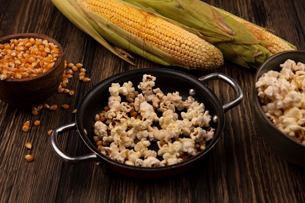 top view of pan with popcorns with corn kernels with fresh corns isolated on a wooden bowl on a wooden table - Воздушная кукуруза (попкорн)