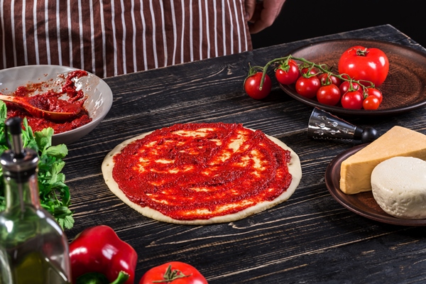 a male hand spreading tomato puree on a pizza base with spoon on an old wooden background cooking concept close up - Пицца "Маргарита"