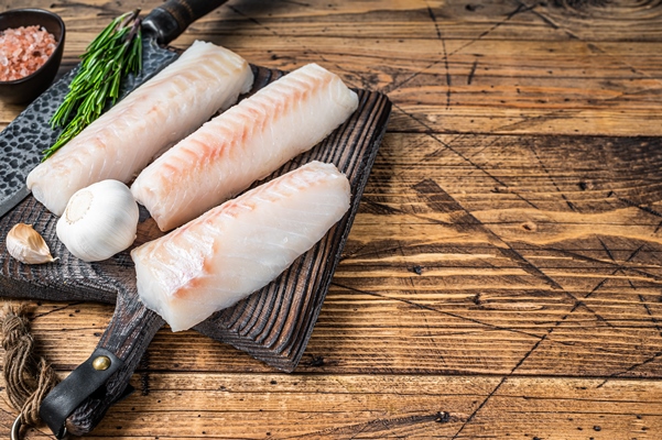 fresh raw cod loin fillet steaks on wooden board with butcher knife wooden background top view copy space - Белая рыба, запечённая с овощами
