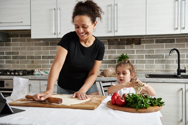 mother and daughter cook pizza together roll out the dough with a wooden rolling pin and have fun together in the kitchen - Пицца постная