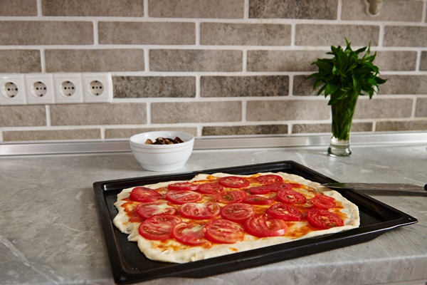 roll out dough with tomato sauce and chopped tomatoes on a baking sheet in the kitchen counter - Пицца постная