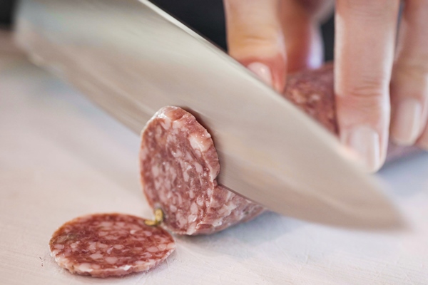 slicing salami into thin rings ona white cutting board - Пицца из кабачков с колбасой