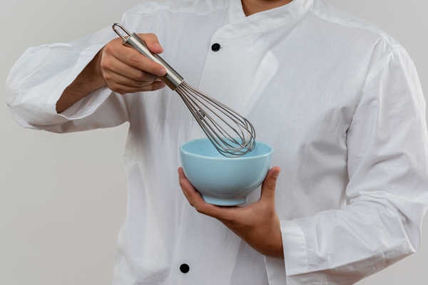 confident young male cook in chef uniform holding whisk and bowl looking isolated on white wall with copy space - Полевка с ржаной мукой