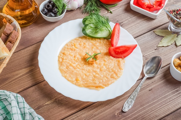 delicious appetizing pea porridge garnish with fresh vegetables on a white plate on a wooden background - Логаза