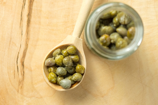 pickled or marinated green capers on a wooden spoon close up selective focus - Пицца с морепродуктами