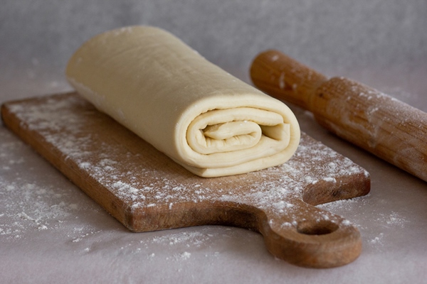 rolled raw homemade puff pastry on the kitchen board - Бульон красный со слоёными мясными пирожками