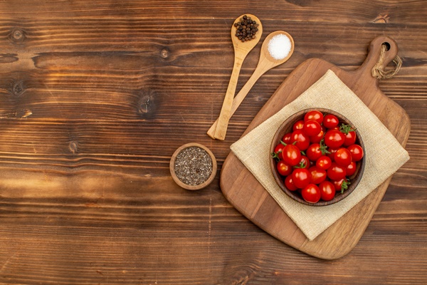 top view of fresh tomatoes on a brown bowl on cutting board and spices in spoons pepper on wooden board - Пицца постная на тонком тесте