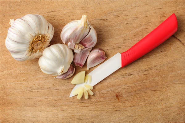 top view of garlic bulb and cloves one cut into small pieces with red ceramic knife placed on old cutting board with many scratches - Тавранчук из говядины