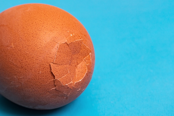 brown cracked egg on a blue background - Секреты приготовления яиц всмятку, "в мешочек" и вкрутую. Пошаговая инструкция