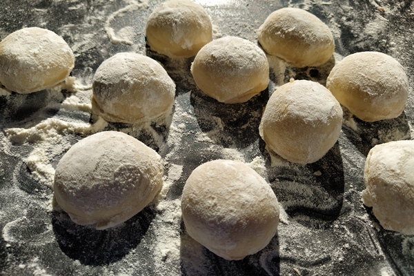 round pieces of shortbread dough for making cookies or gingerbread raw buns or dumplings with scattered flour around on black background - Орешки со сгущёнкой