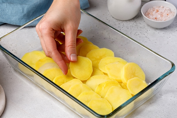 step by step recipe of potato gratin hands stack potato slices to glass baking dish potato casserole - Картофель, запечённый с лососем