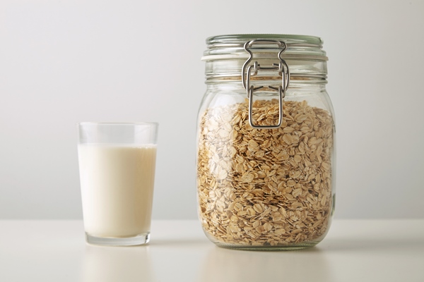 transparent glass with fresh organic milk near rustic jar with rolled oats isolated in center on white table - Кулинарные секреты для одиноких