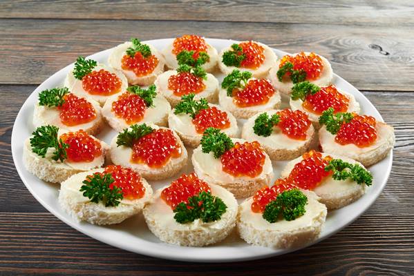 white plate on the wooden table full of little canapees with butter red caviar and decorated with fresh green parsley leaves tasty appetizer foe alcohol catering or restaurant buffet - Рекомендации по расчёту банкетных блюд и напитков