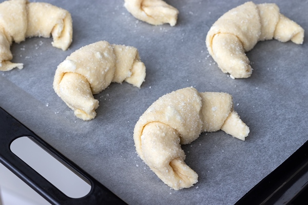 croissants from a raw cottage cheese dough prepared for baking sprinkled with sugar on a baking sheet covered with parchment baking paper before loading into the oven process of making curd bagels - Рогалики по ГОСТу