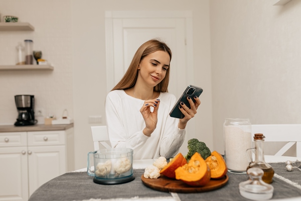 european woman with light brown hair is laughing and looking recipe in smartphone young lady preparing for cooking with pumpkin and broccoli - Пирамида питания