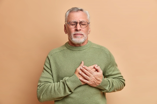 mature man presses hands to heart has cardio problems suffers heart attack and chest pain stands with closed eyes needs doctors help wears casual jumper isolated over brown wall - О вреде крабовых палочек