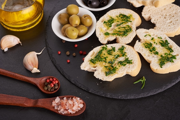 mediterranean snacks set olives oil herbs and sliced ciabatta bread on black slate stone board over painted dark blue surface top view flat lay - Средиземноморская диета