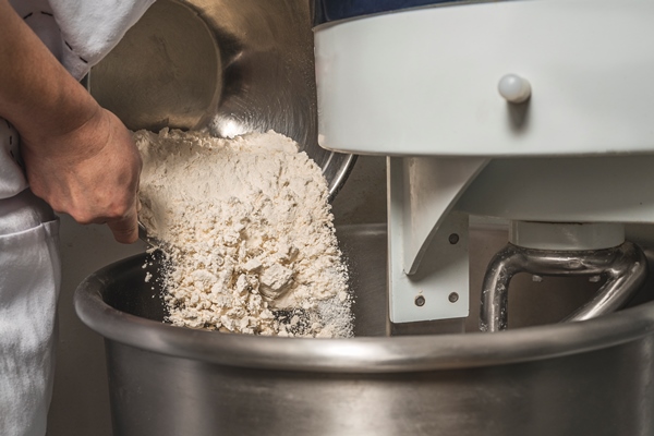 person adding flour in an industrial mixer to make bread - Украинский хлеб