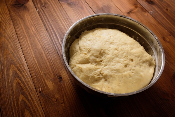 raw yeast dough resting and rising in large metal bowl on dark wooden background - Рогалики по ГОСТу