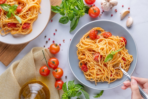 tasty appetizing classic italian spaghetti pasta with tomato sauce cheese parmesan and basil on plate and ingredients for cooking pasta on white marble table flat lay top view copy space - Средиземноморская диета