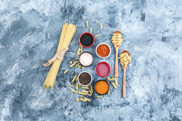 top view raw pasta with spices wooden spoons on grey plaster background horizontal - Средиземноморская диета