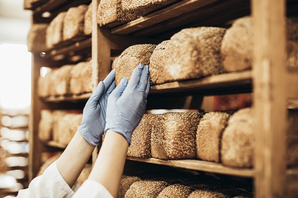young female worker working in bakery she puts bread on shelf - Ржаной столовый хлеб
