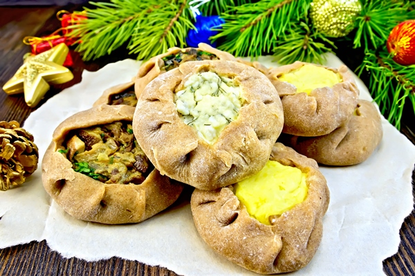 carols of rye flour filled with cheese potatoes and mushrooms on paper christmas decorations fir branches on the background of wooden boards - Святочные кулинарные традиции. Гусь с яблоками