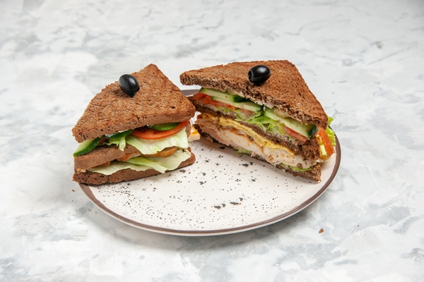front close view of delicious sandwich with black bread decorated with olive on a plate on stained white surface - Использование оливок в кулинарии