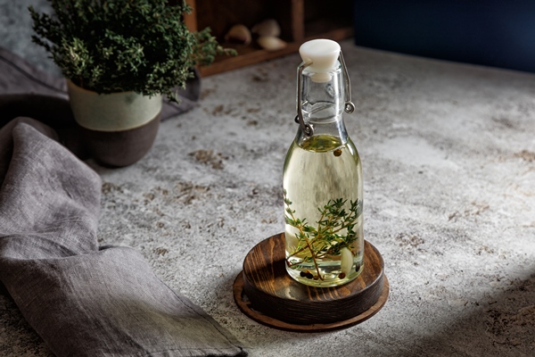 glass bottle of oil with thyme and garlic and pepper on a gray background with a napkin - Использование оливок в кулинарии