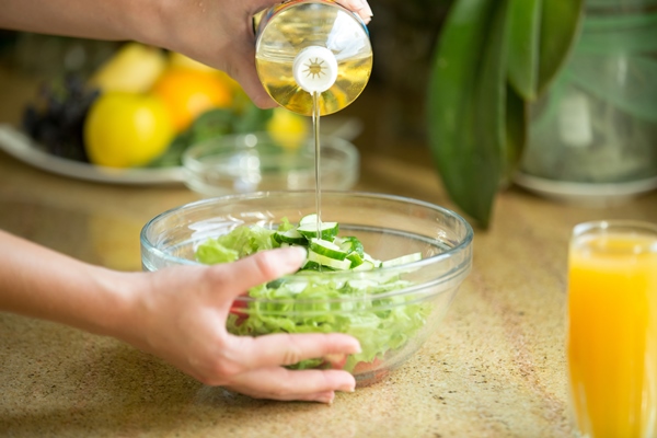 hands pouring oil in a green salad - Использование оливок в кулинарии