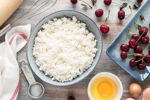 ingredients for making cottage cheese dumplings with cherries cottage cheese egg flour and fresh cherries on a wooden table vertical - Сырники с манкой
