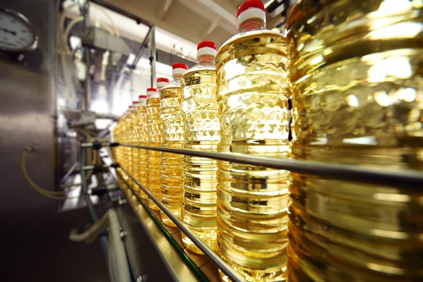 line or conveyor for food production of sunflower oil bottles with vegetable oil close up against the surface of factory equipment - Оливковое масло