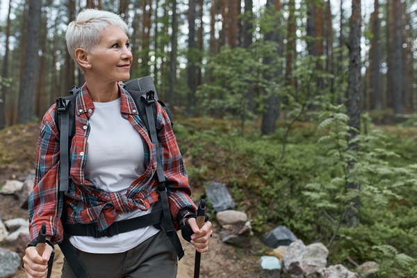 outddor portrait of happy european female pensioner with backpack and poles enjoying beautiful nature while nordic walking in pine forest - Бородинский хлеб: история и современность