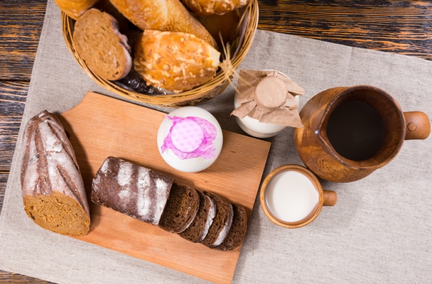 overhead view of a large selection of breads and sliced pumpernickel beside two jars of milk and an wooden jug - Бородинский хлеб: история и современность