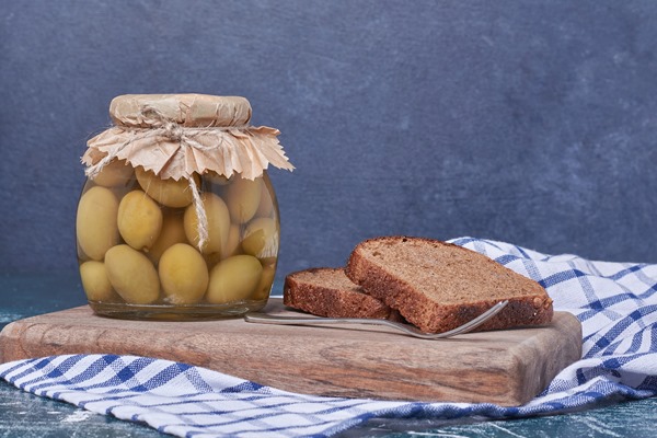 pickled olives in glass jar with black bread slices on blue - Оливки и маслины: в чём разница