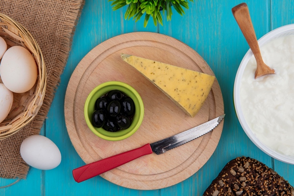 top view cheese with olives and a knife on a stand with yogurt in a bowl on a turquoise background - Использование оливок в кулинарии