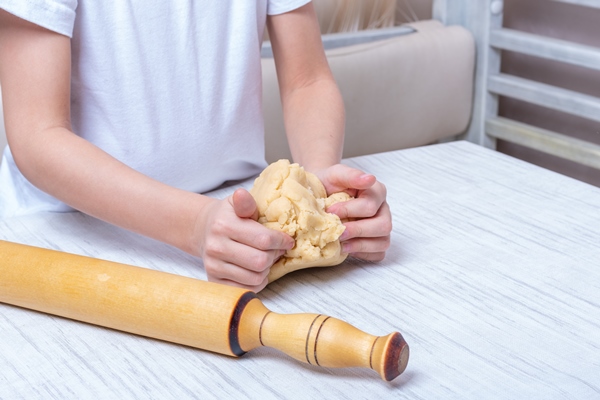 children s hands roll out the dough with a rolling pin on the table in the kitchen little kid helps mother to cook making homemade coockies - Тесто на кефире для пельменей и вареников