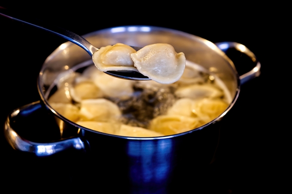dumplings mixed with a spoon in a pot of boiling water boiled dumplings in a pan black background close up - Домашние пельмени из заварного теста