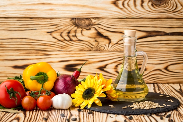glass bottle of sunflower oil on a wooden table with a composition of vegetables and seeds - Блинцы заварные на кефире
