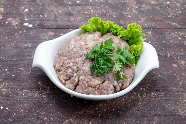 minced raw meat with greens inside plate on brown - Русские пельмени