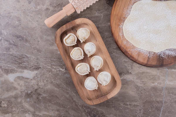 raw dumplings on wooden board with dough and flour on marble table - Пельмени с рыбной начинкой
