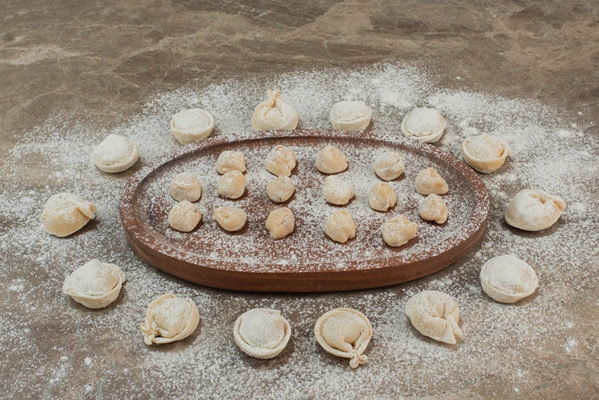 raw dumplings on wooden board with flour - Пельмени