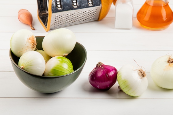 side view of onions in bowl with other ones butter salt grater on wooden background - Цеппелины