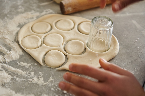 the woman cuts out the round moulds with a glass for ravioli or dumplings focus on dough - Пельмени