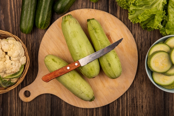top view of zucchinis isolated on a wooden kitchen board with knife with cauliflower on a bucket with cucumbers and lettuce isolated on a wooden surface - Пельмени